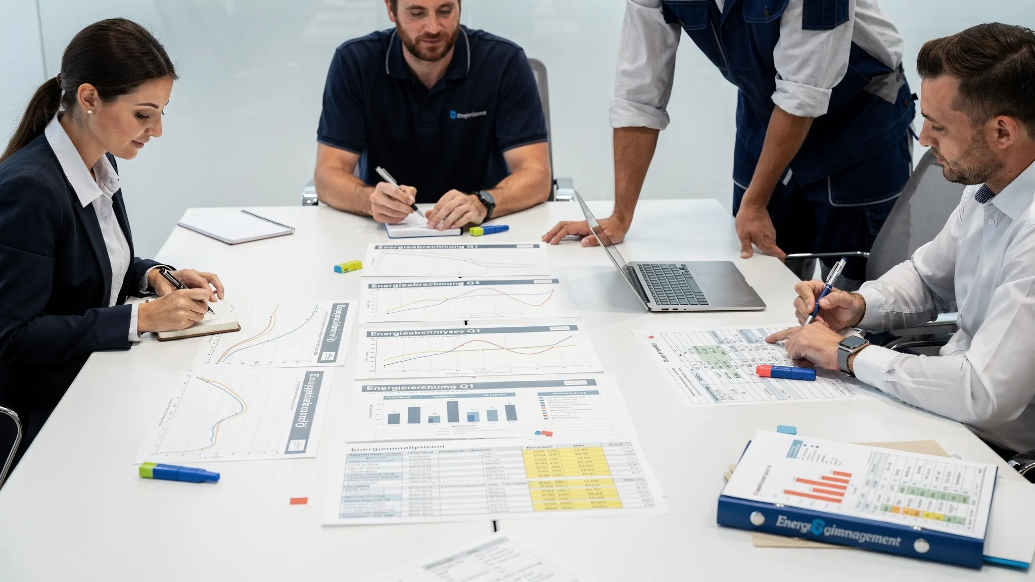 Ein Besprechungstisch mit ausgedruckten Lastgangkurven, Energieabrechnungen und Produktionsplänen; Vertreter aus Einkauf, Betrieb, Controlling und Energiemanagement markieren gemeinsame Entscheidungen und Maßnahmen.